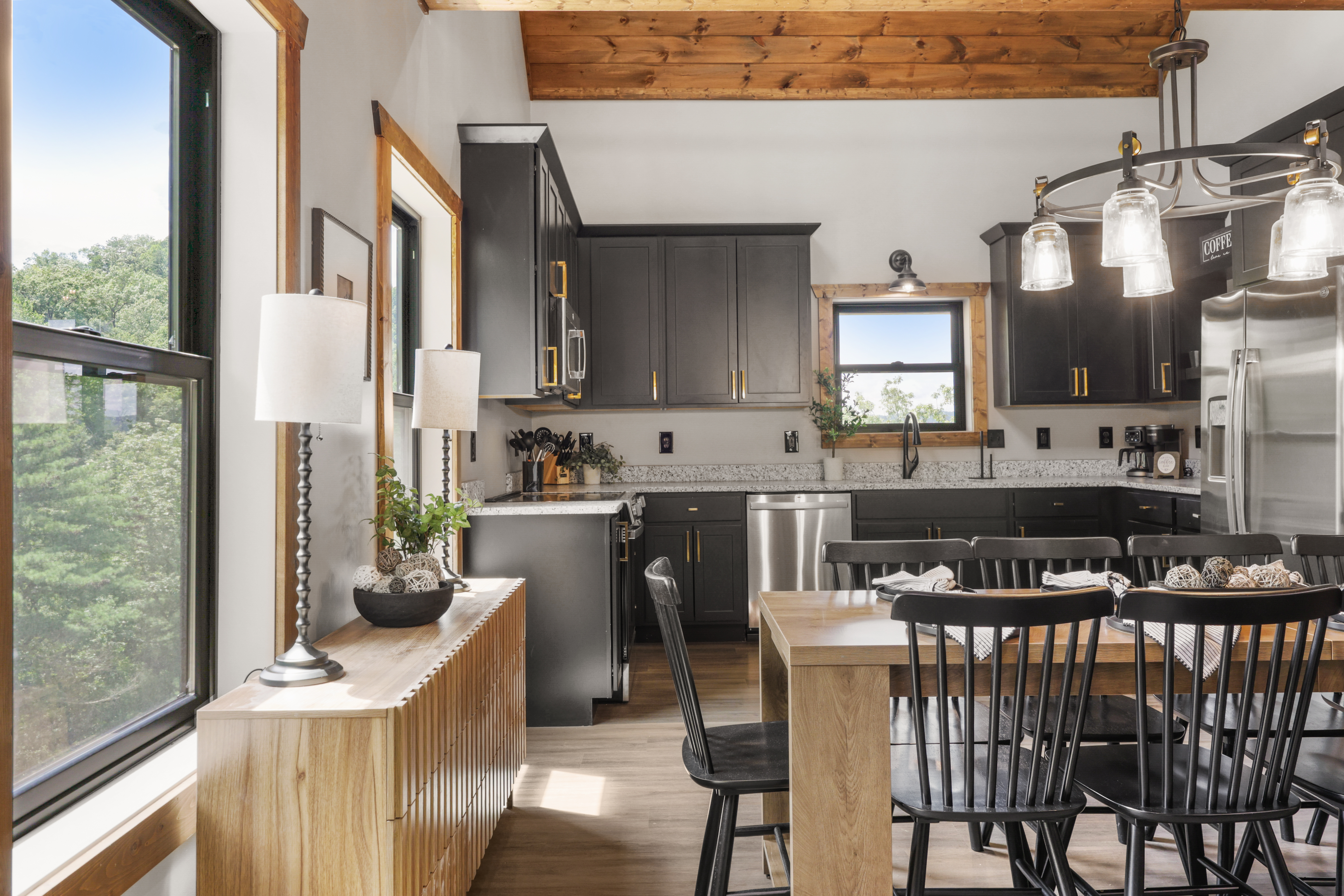 Bright rustic-modern kitchen with wood beams, dining space, and forest views