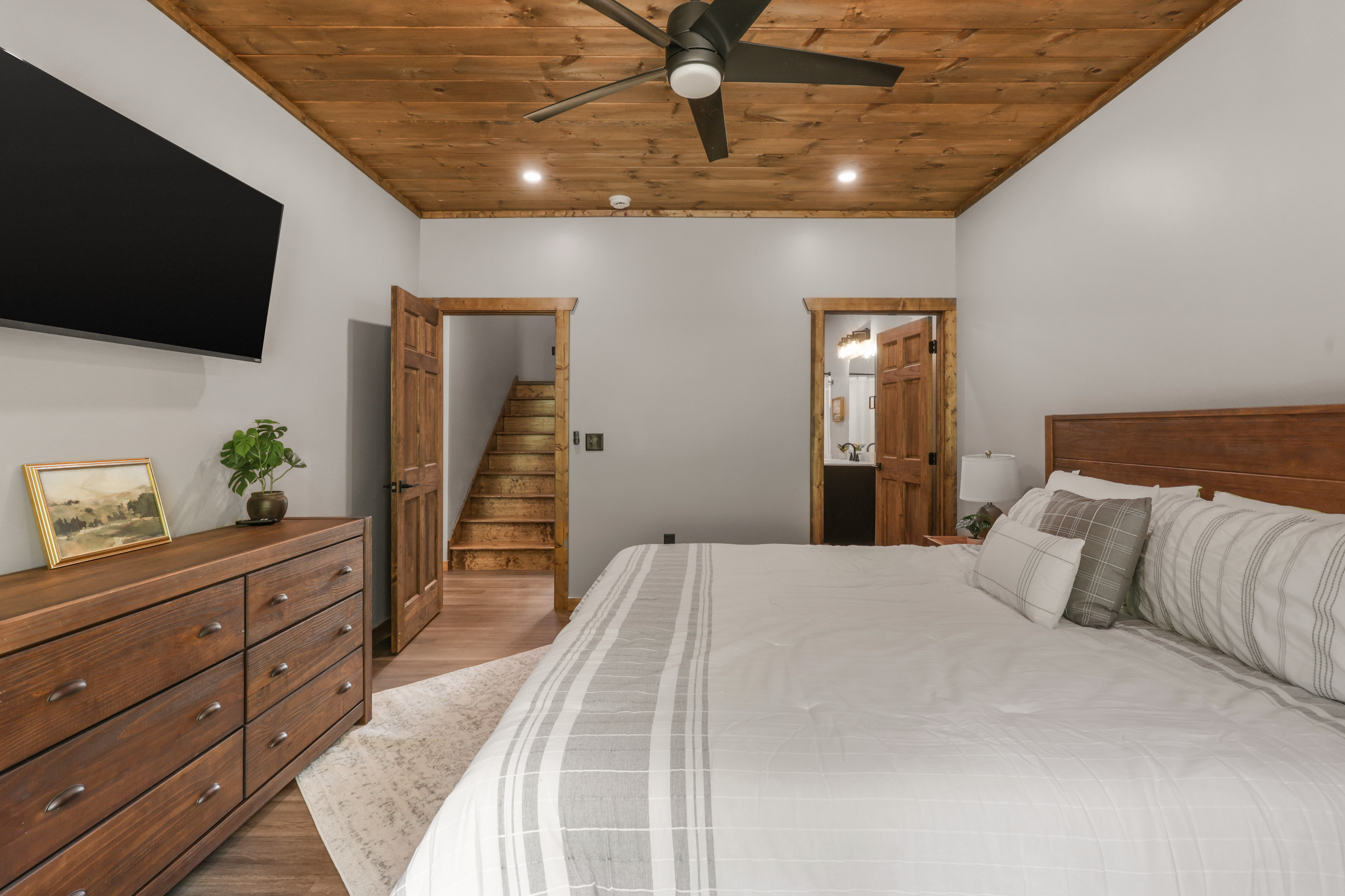 Cozy king bedroom with wood ceilings, TV, and warm rustic-modern style