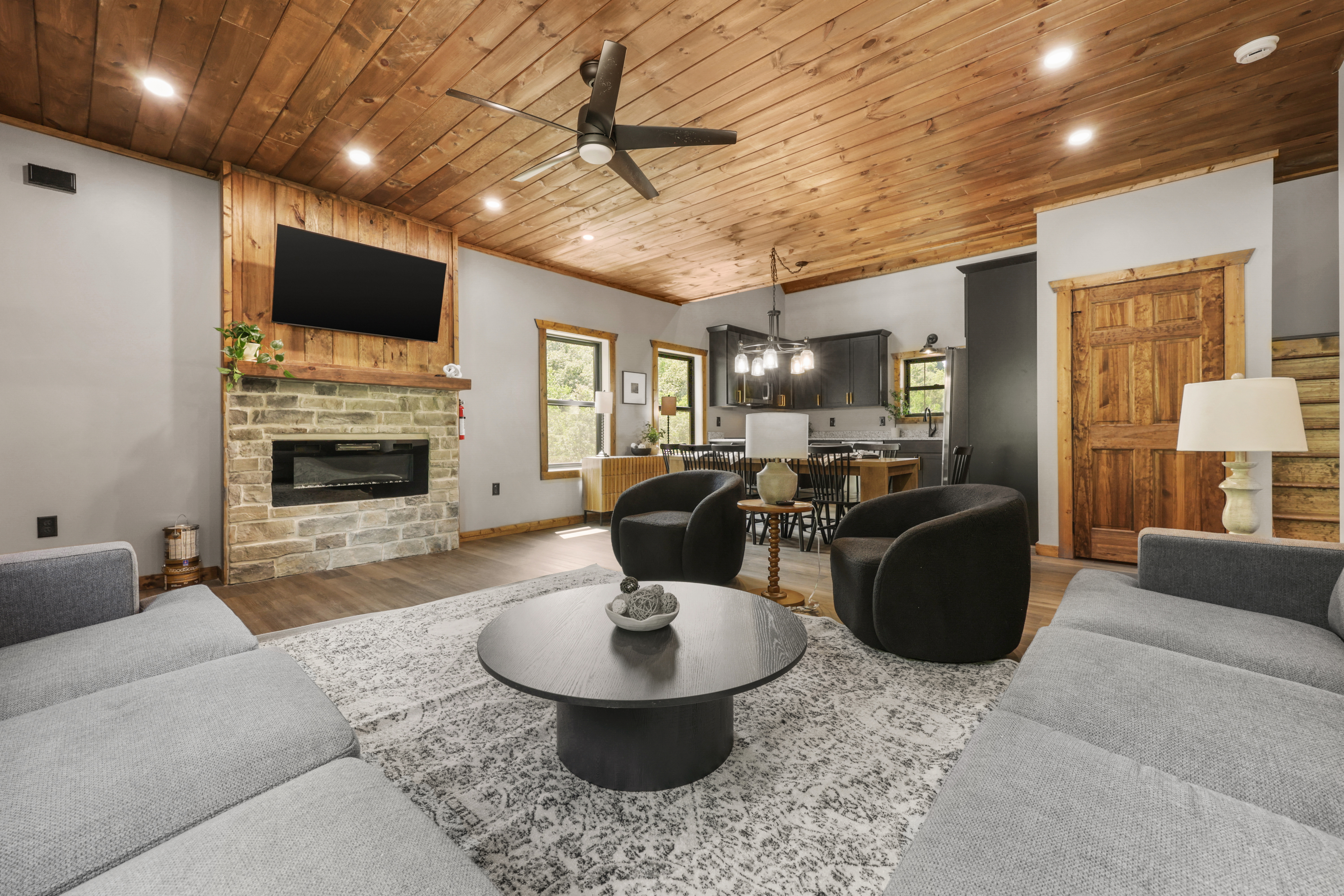 Cozy open living room with stone fireplace, TV, and warm cabin-style charm
