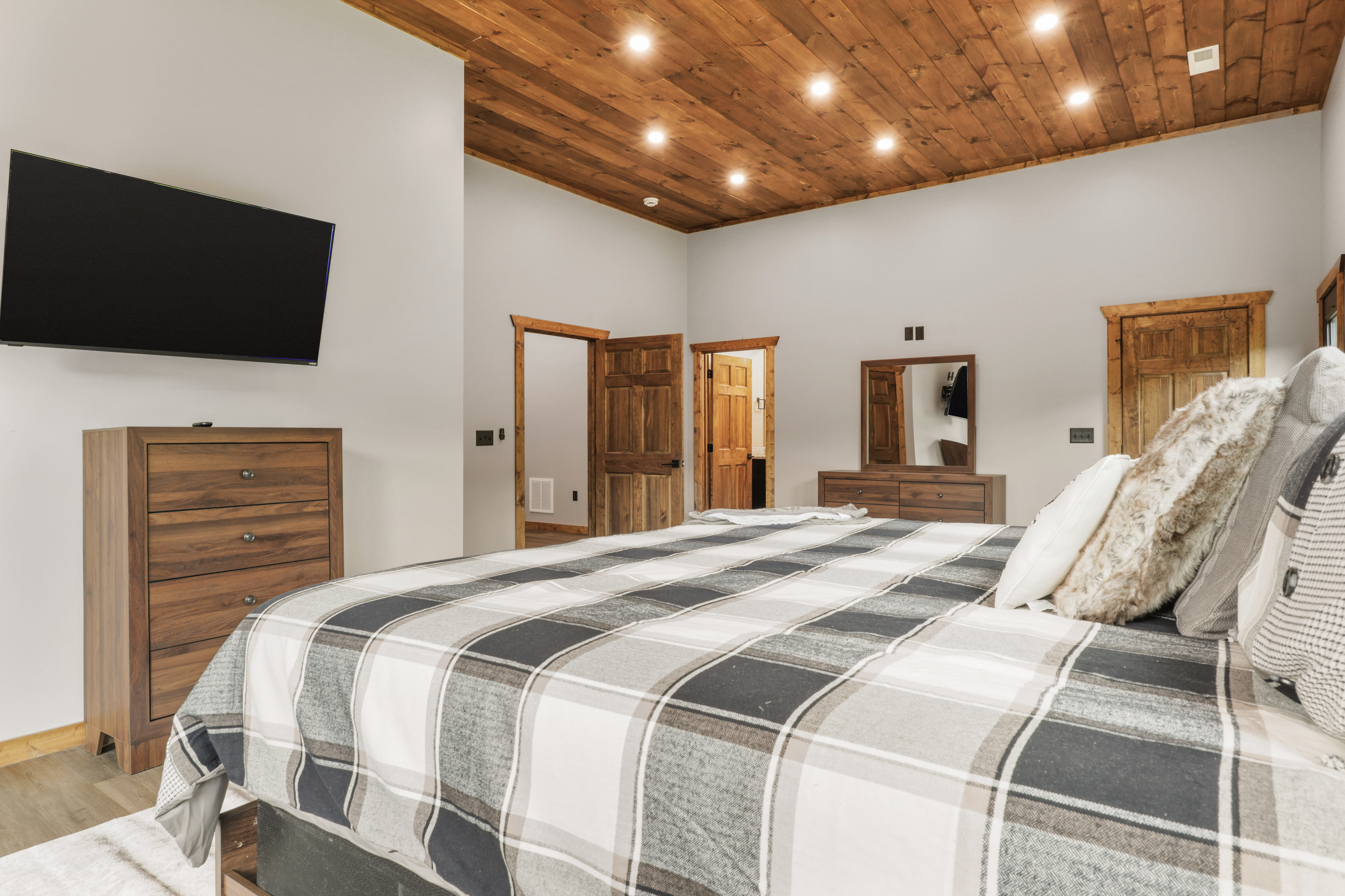 Spacious rustic bedroom with wood ceilings, cozy king bed, and TV