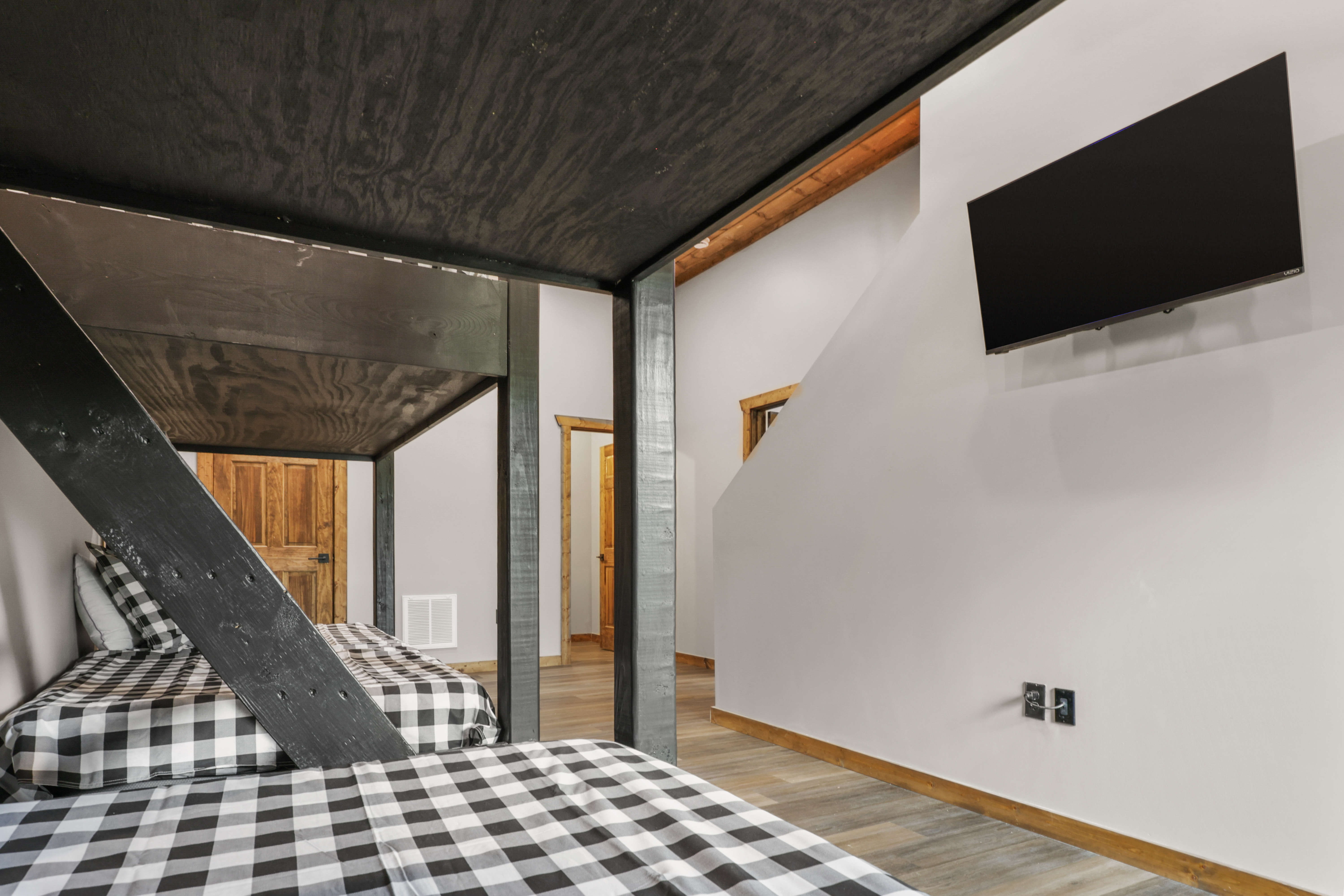 Cozy loft sleeping space with twin beds, rustic beams, and wall-mounted TV