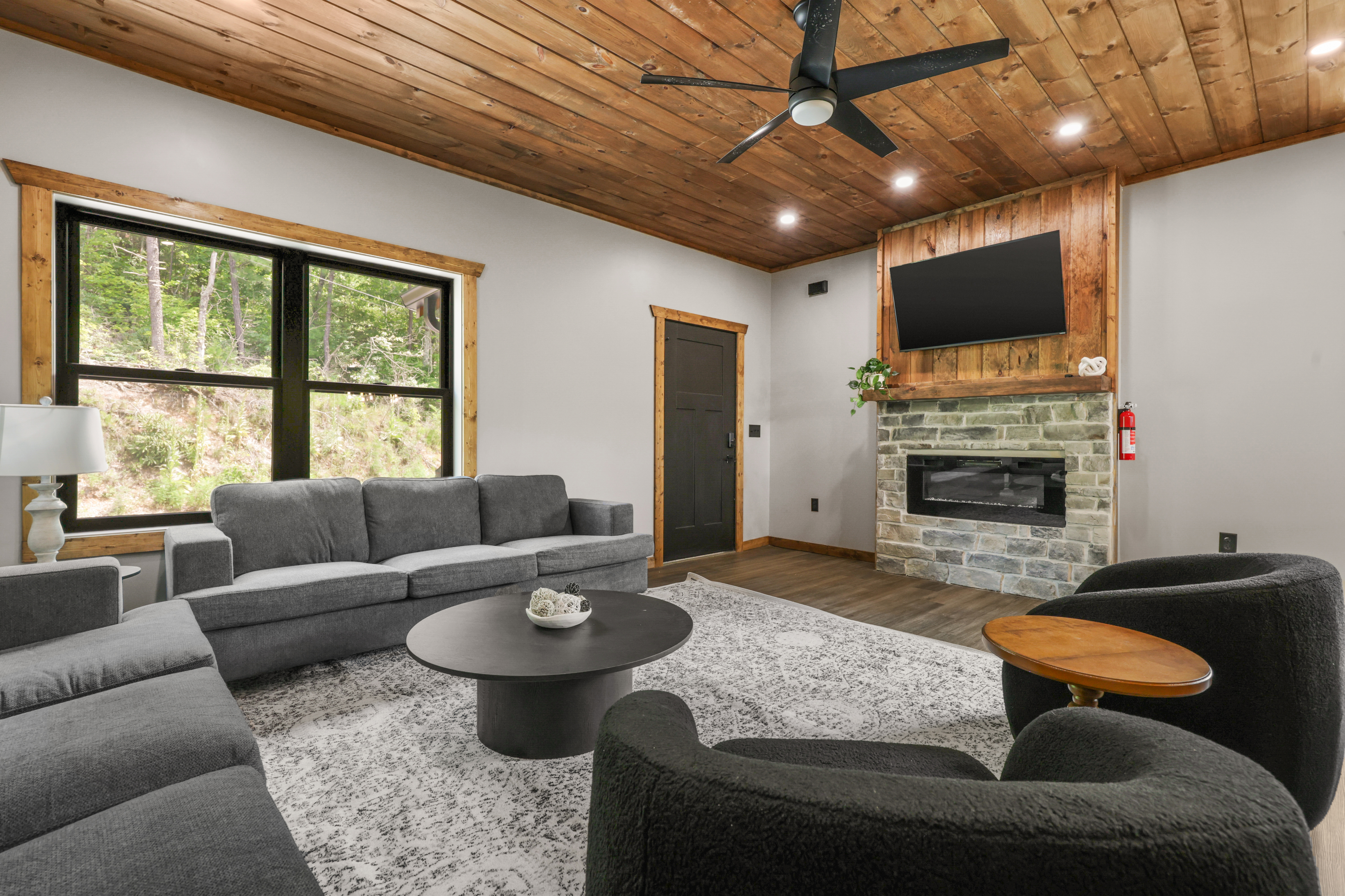 Cozy modern lounge with stone fireplace, TV, and peaceful forest views