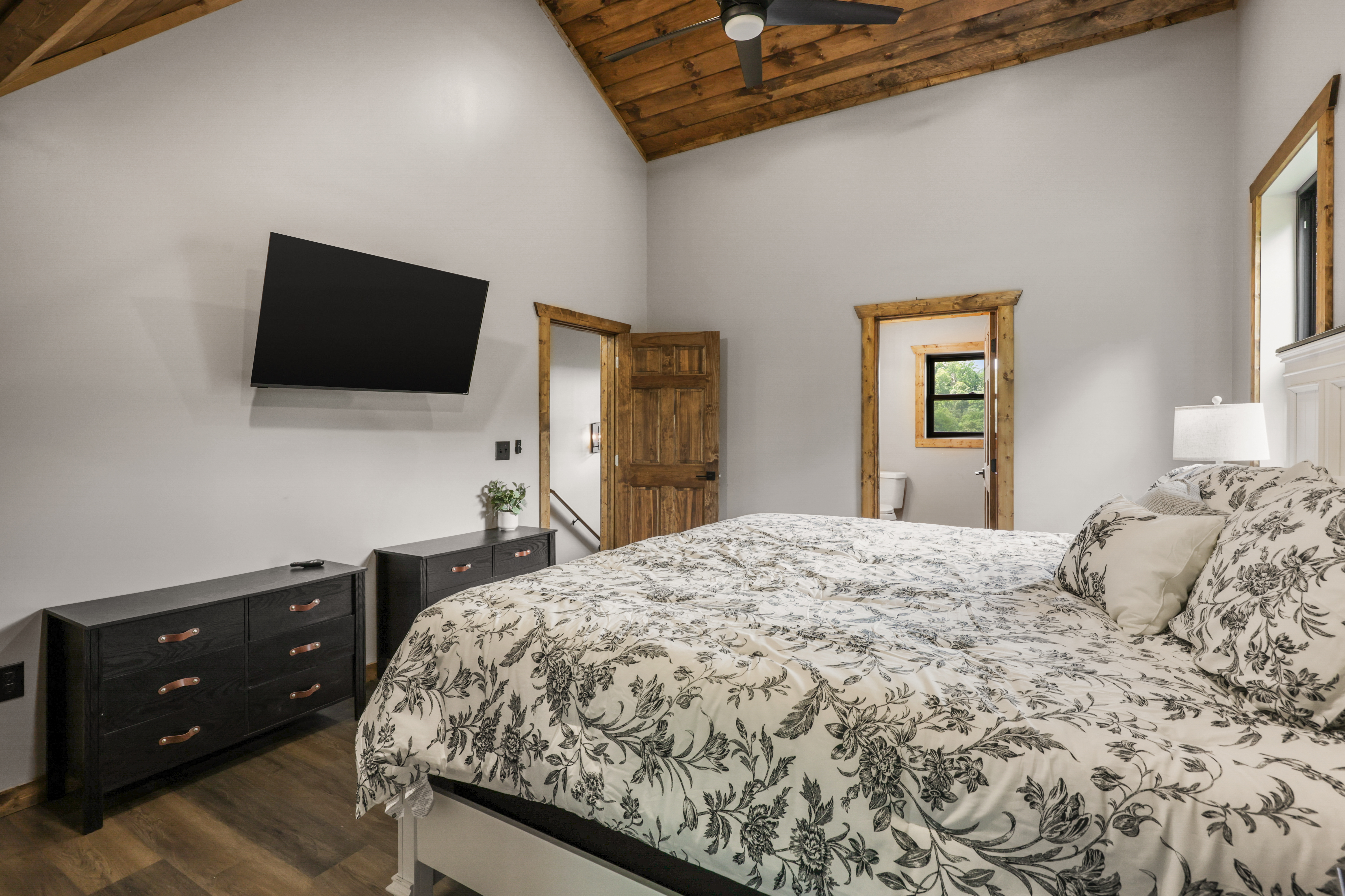 Bright rustic bedroom with vaulted ceilings, TV, and en suite bath access