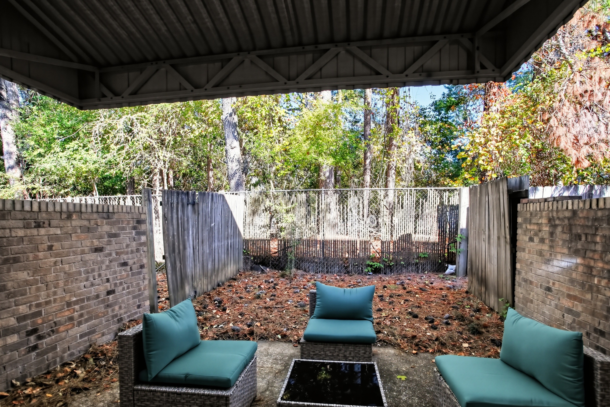 Private covered patio with cozy seating and a peaceful wooded backdrop