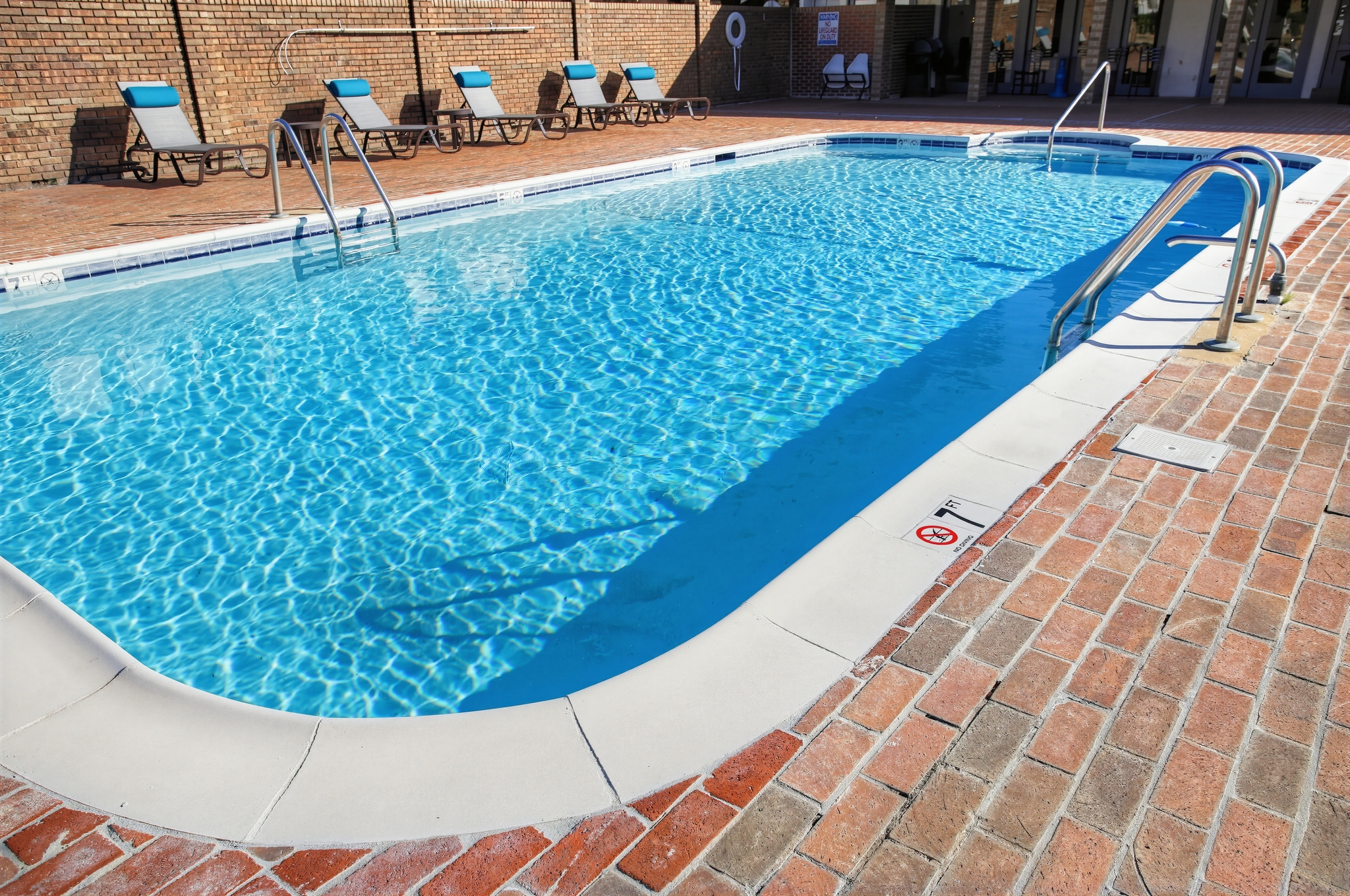 Sunny outdoor pool with lounge chairs and spacious brick deck