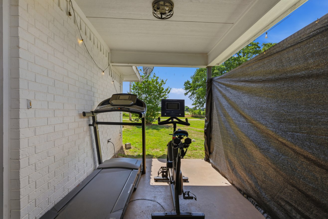 Covered outdoor workout space with treadmill, bike, and yard views