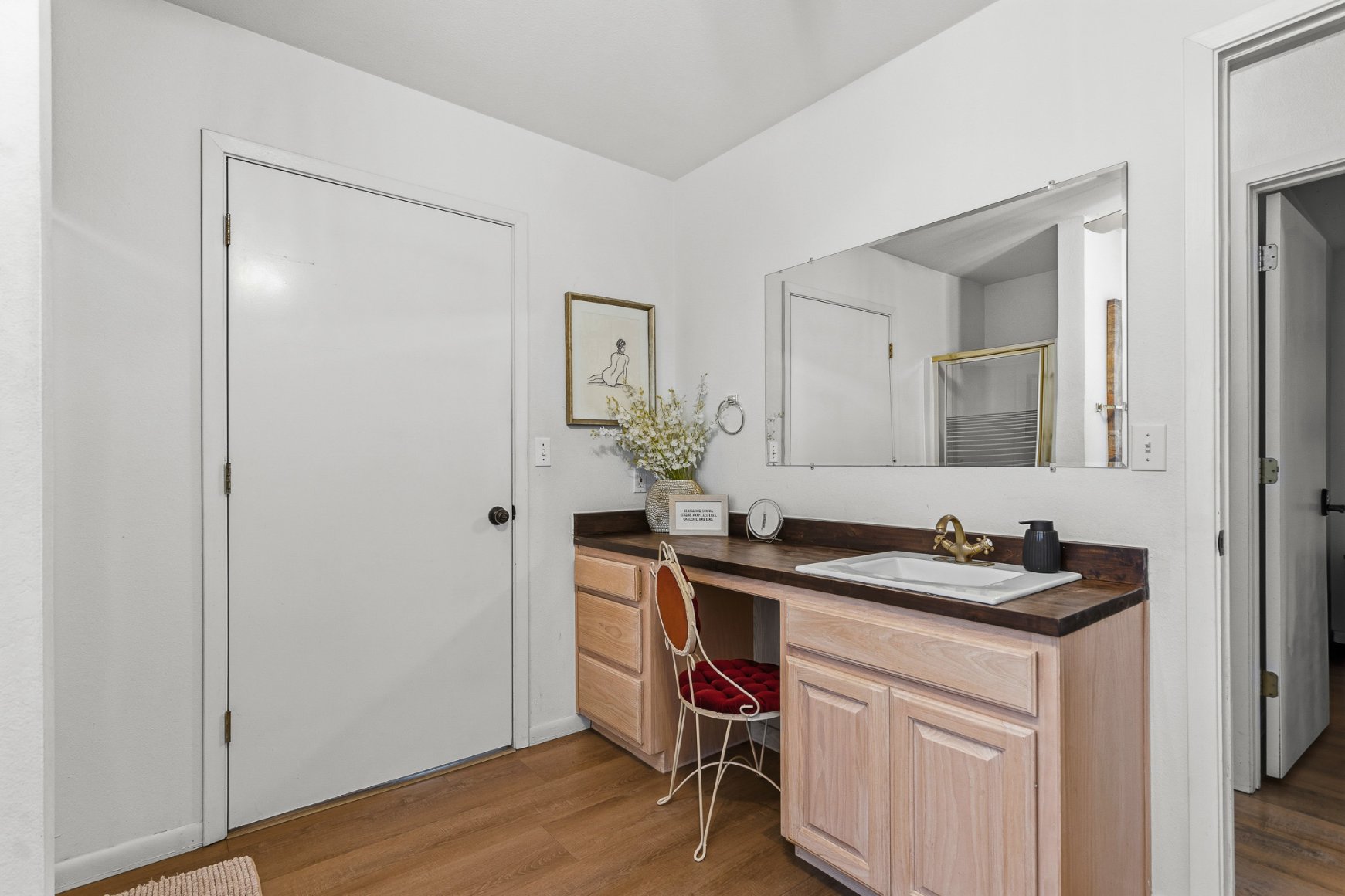 Bright vanity area with large mirror, warm wood finishes, and charming seating
