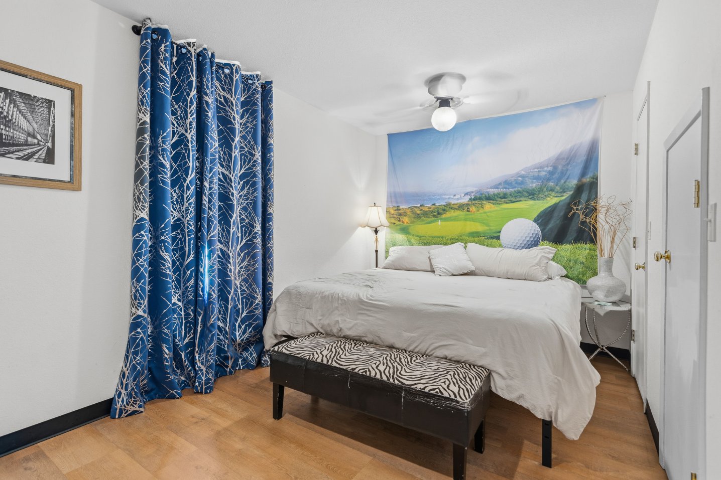 Bright, cozy bedroom with scenic wall art and bold blue accents
