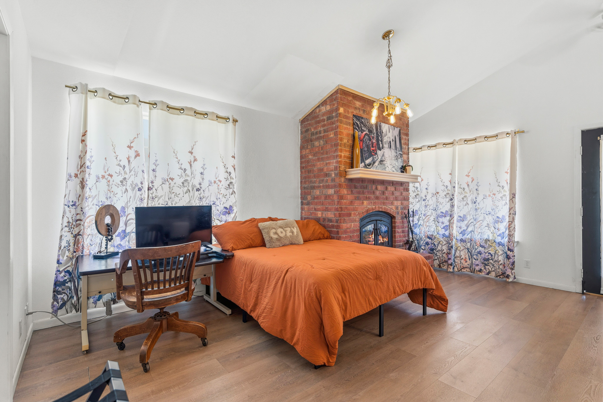 Spacious sunlit bedroom with brick fireplace, workspace, and cozy charm