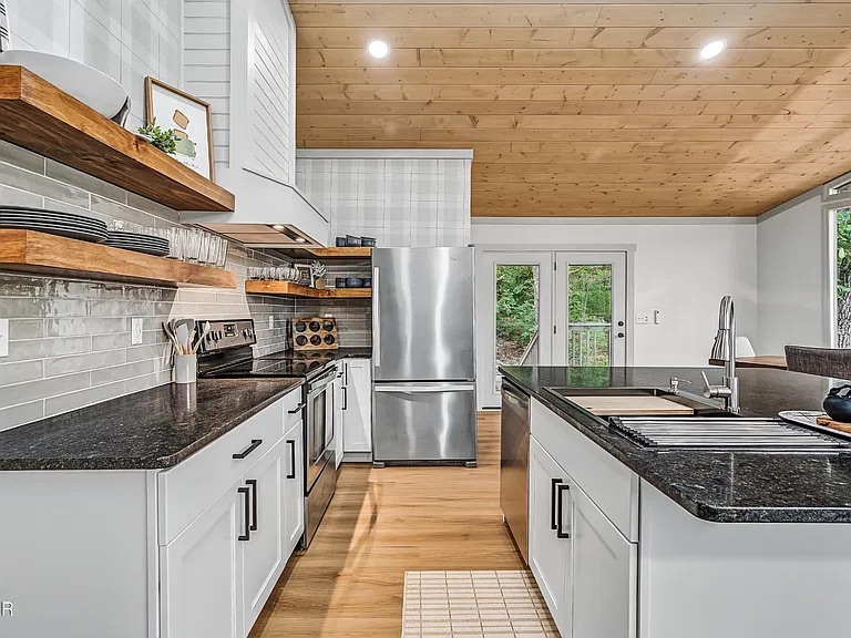 Bright modern kitchen with island, open shelving, and forest views