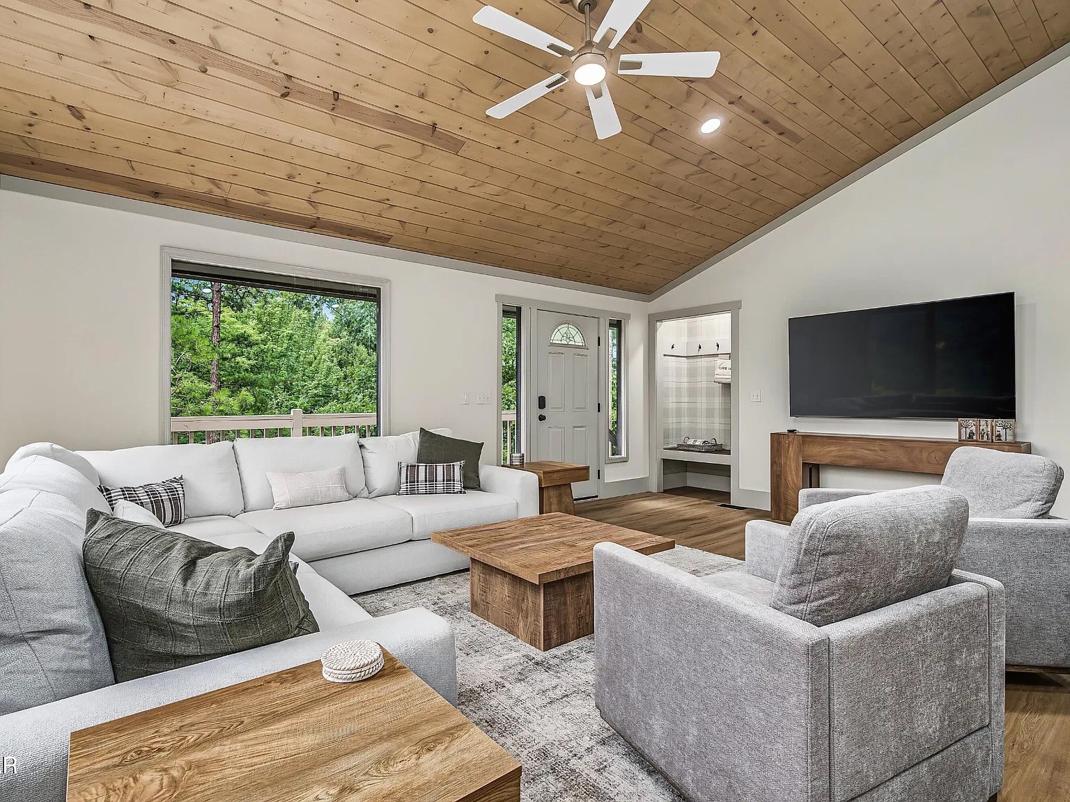 Bright great room with vaulted wood ceiling, forest views, and cozy seating