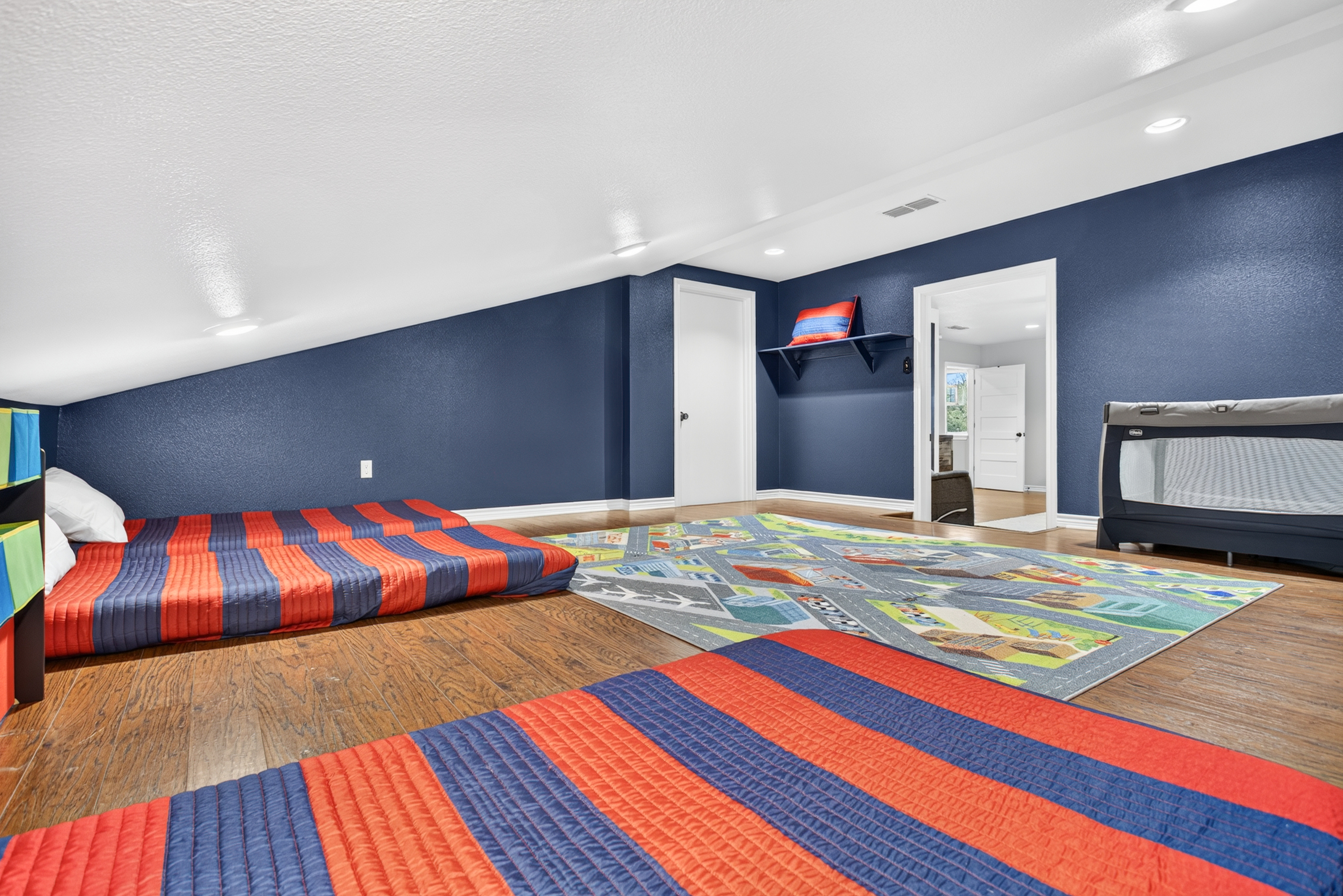 Fun loft-style kids’ room with play rug, floor beds & travel crib