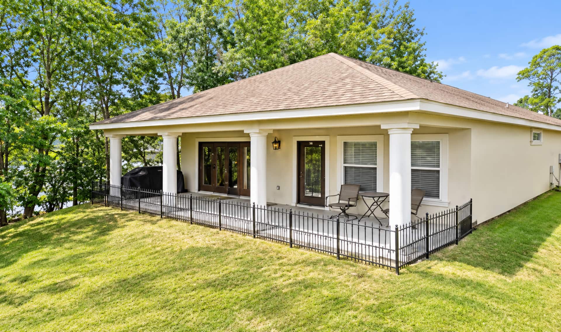 Spacious covered patio with grill, seating, and peaceful tree-lined yard