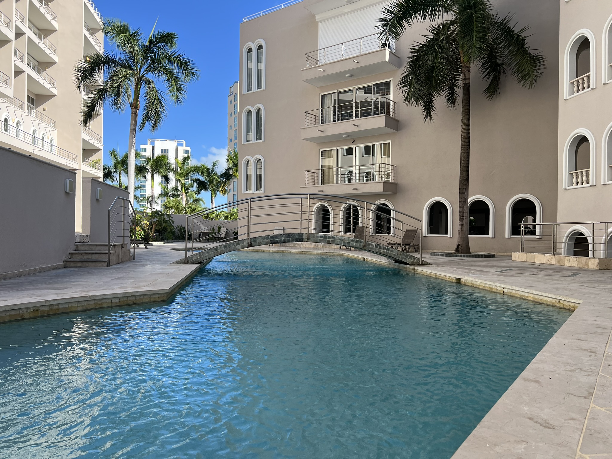 Resort-style pool with palm trees, sun deck, and charming bridge