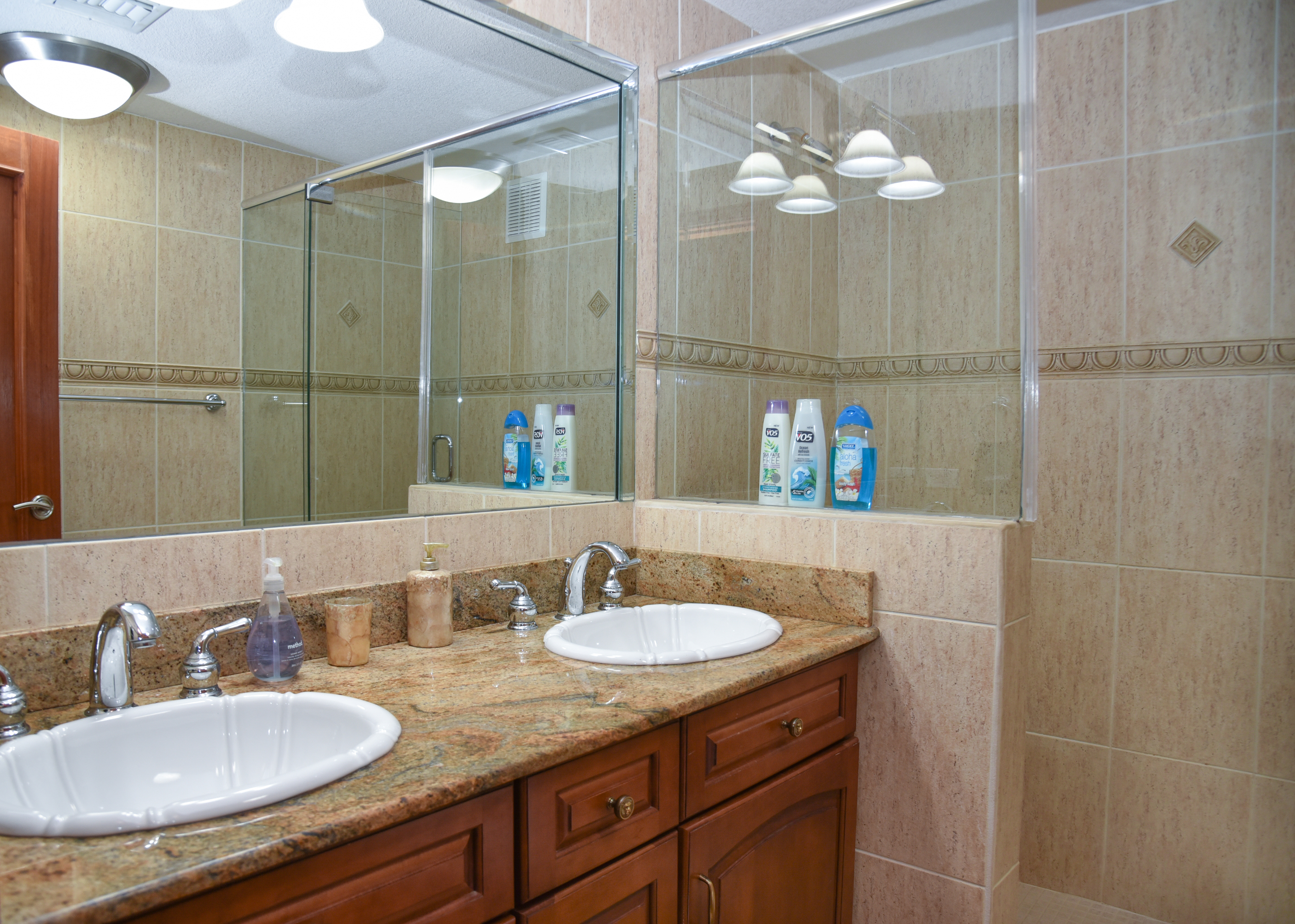 Bright double-vanity bathroom with granite counters and glass shower
