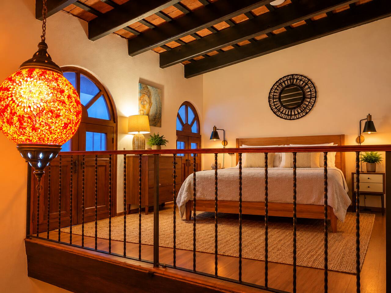 As evening falls, warm lighting transforms the upstairs queen loft into a cozy retreat. Exposed wooden beams, charming arched windows, and a glowing Turkish lamp capture the romance and historic character of Old San Juan.