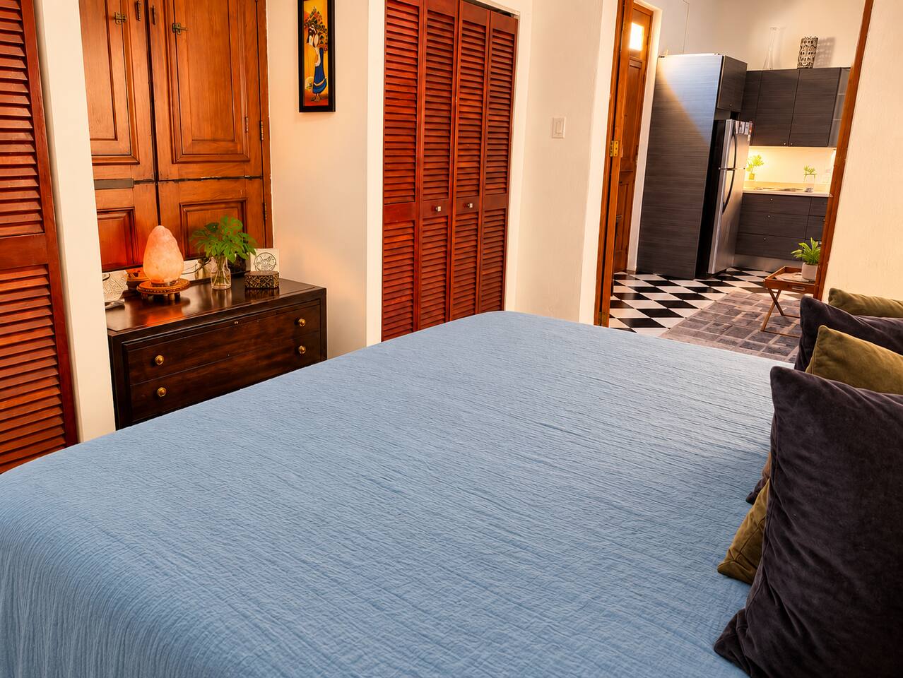 Relax in this inviting bedroom featuring a comfortable king bed with soft blue bedding, rich wooden shutters, charming vintage furnishings, air conditioning, and a ceiling fan.
