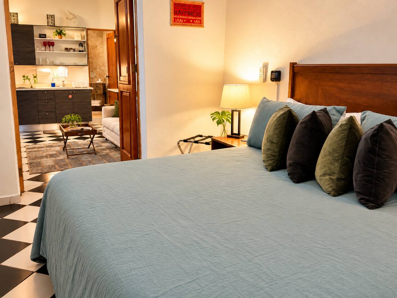 Unwind in this inviting bedroom featuring a comfortable king bed, soft blue bedding, and warm lighting. The rich wood headboard and colorful accents create a cozy retreat, while the adjoining living area and kitchenette offer extra space to relax.