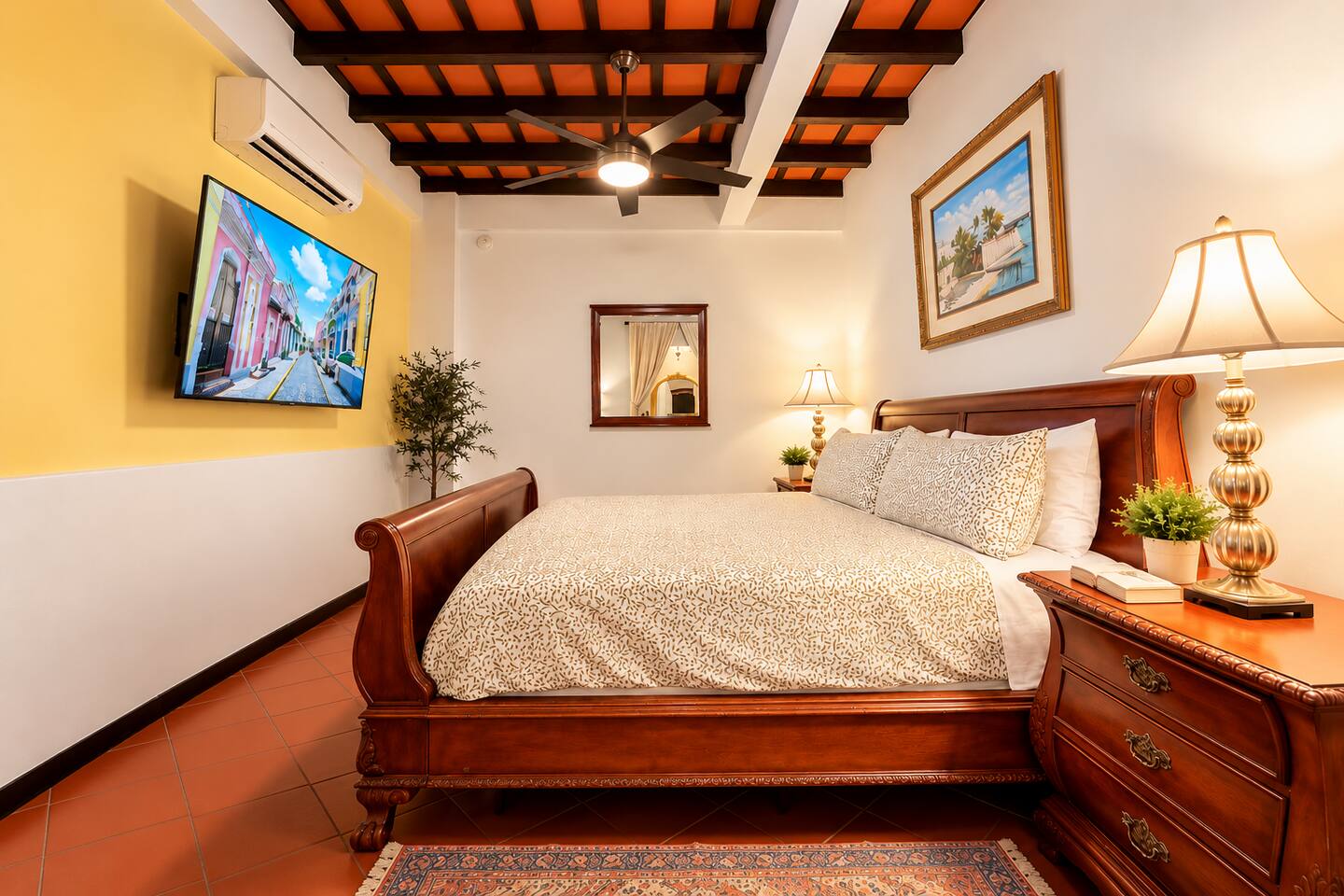Relax in this elegant king bedroom featuring a beautiful carved wood bed, exposed-beam ceilings, & warm Caribbean charm. Enjoy a large Smart TV, quiet air conditioning, ceiling fan, & inviting furnishings for a restful stay in historic Old San Juan.