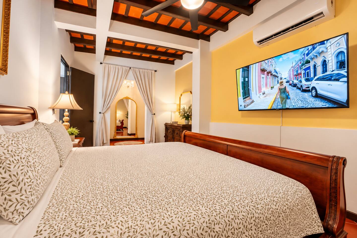 Unwind in this inviting king bedroom featuring beautiful exposed-beam ceilings, elegant furnishings, a large Smart TV, quiet air conditioning, and a ceiling fan. A charming retreat blending modern comfort with the historic character of Old San Juan.