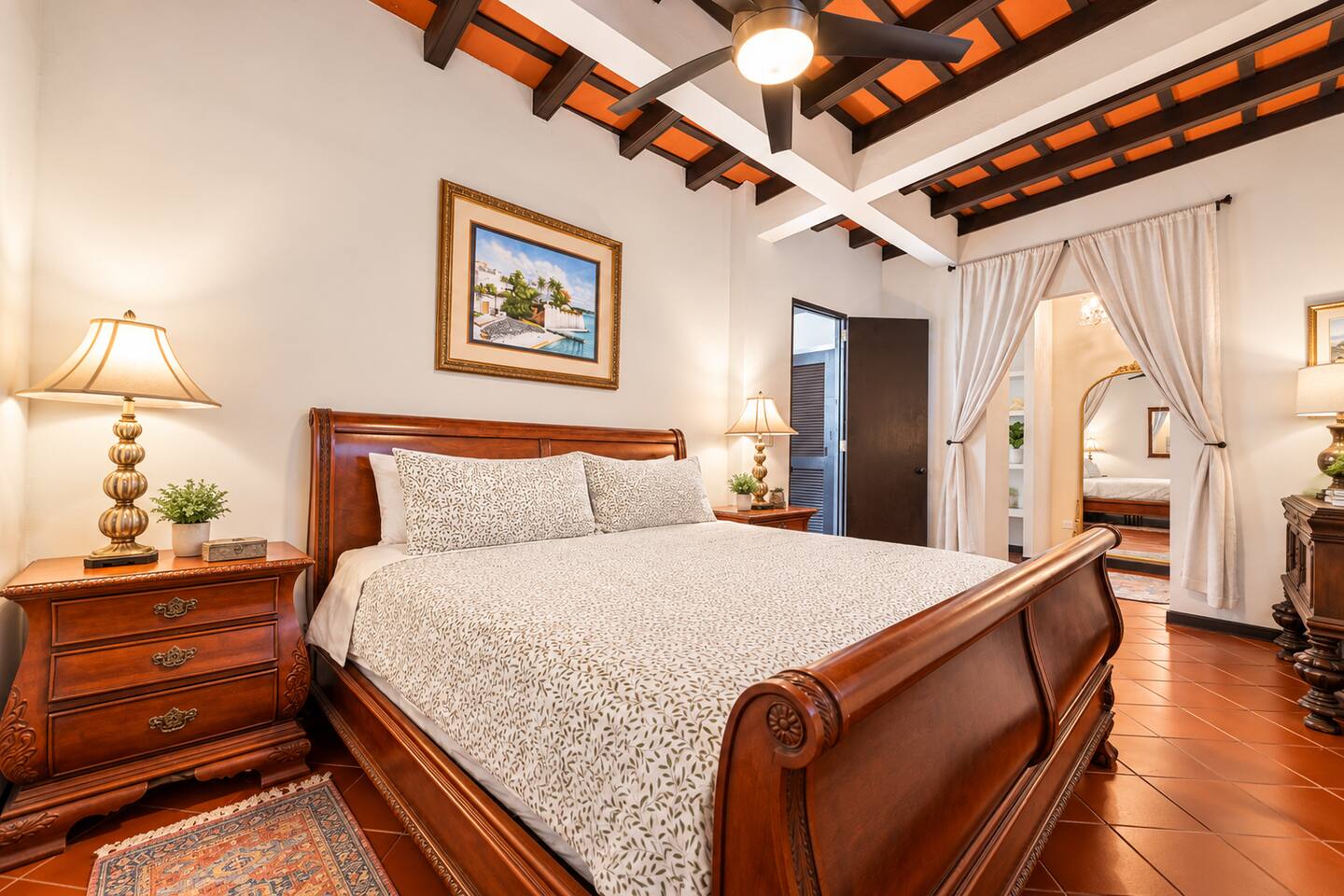 Unwind in this elegant bedroom featuring a beautiful antique sleigh bed, soaring ceilings with exposed beams, quiet A/C, and a ceiling fan. Warm lighting, classic furnishings, and charming architectural details create a peaceful retreat.